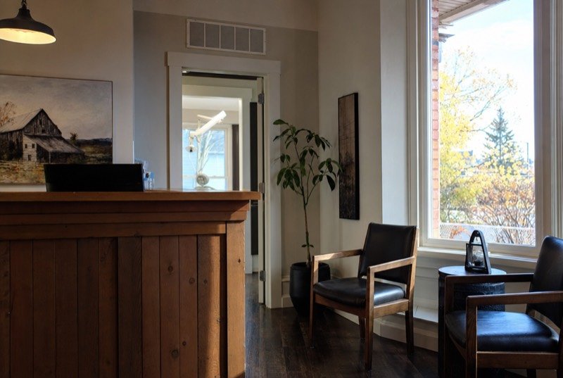 Reception area of a dental clinic with a warm wood counter, soft light and a wide window