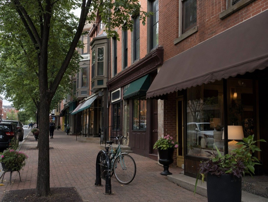 A row of independent shops in red-brick heritage buildings with canvas awnings, flower planters and bicycles locked to posts